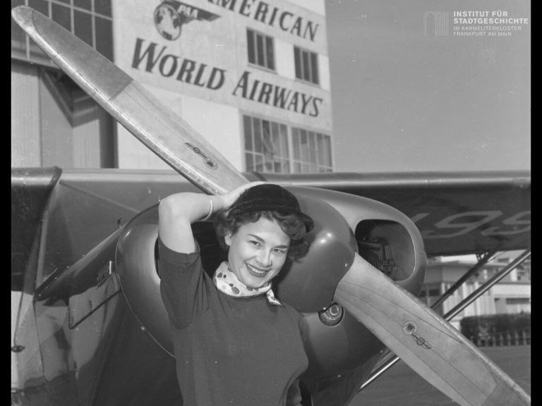 Alte Fotografie, auf der eine Frau vor einem Propeller eines Flugzeugs posiert